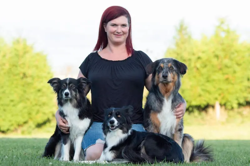 Denise Sättler sitzt mit drei Hunden auf einer Wiese